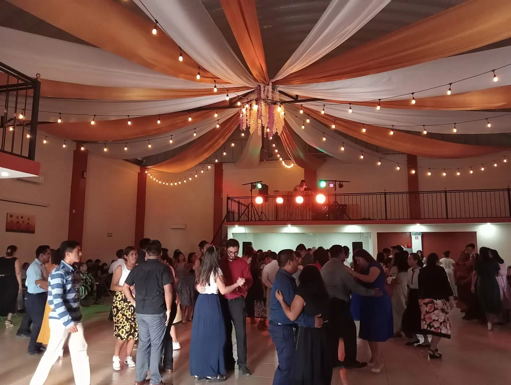 Personas disfrutando de un baile en un salón de eventos iluminado con luces cálidas