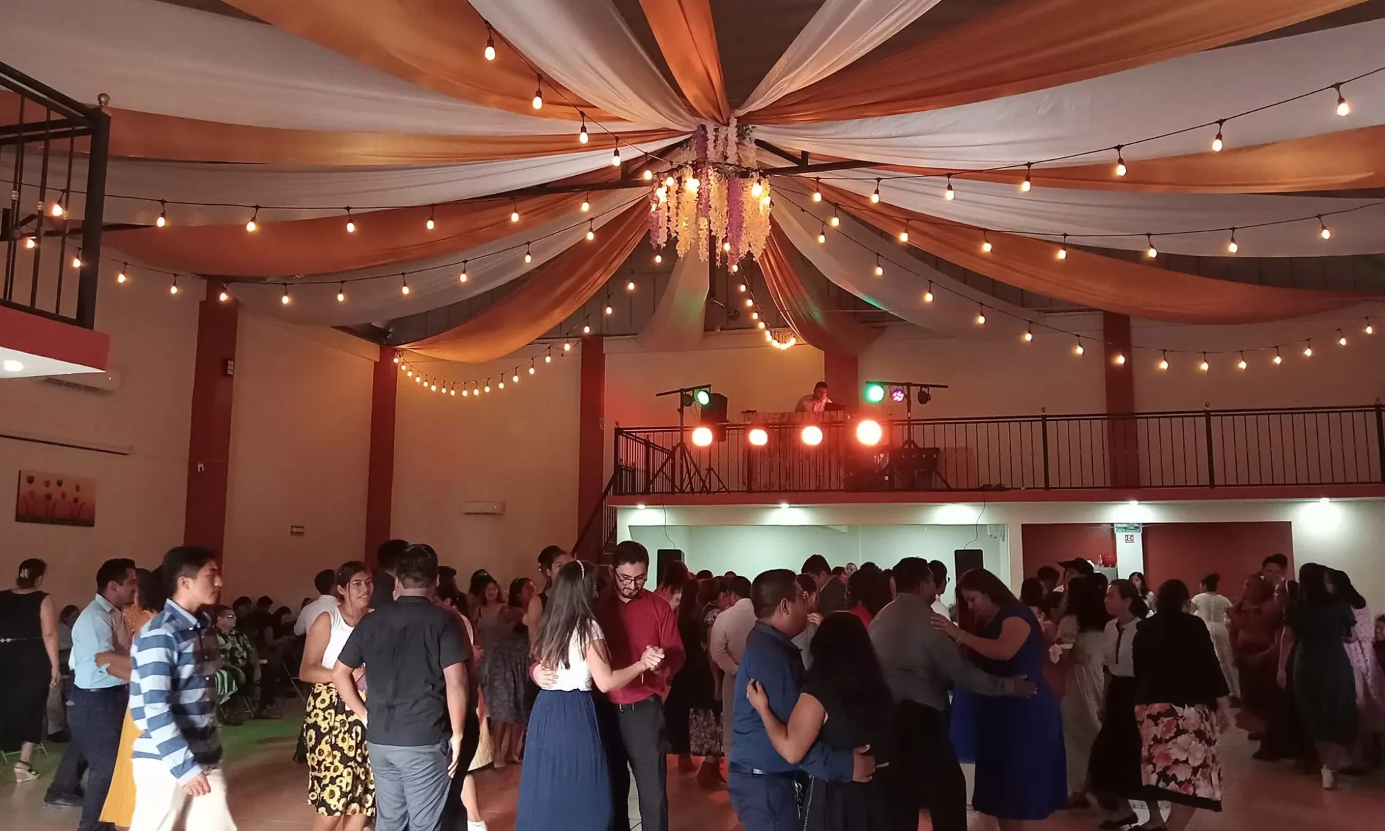 Personas disfrutando de un baile en un salón de eventos iluminado con luces cálidas