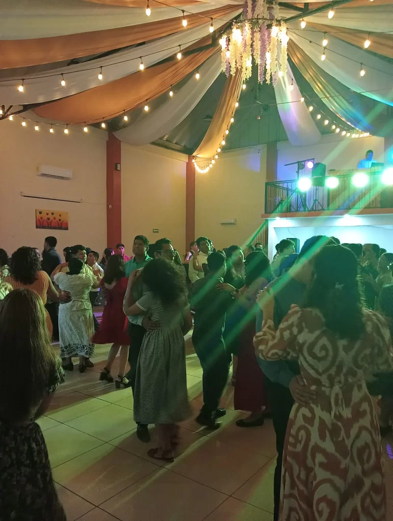 Personas disfrutando de un baile en un salón iluminado con luces de colores