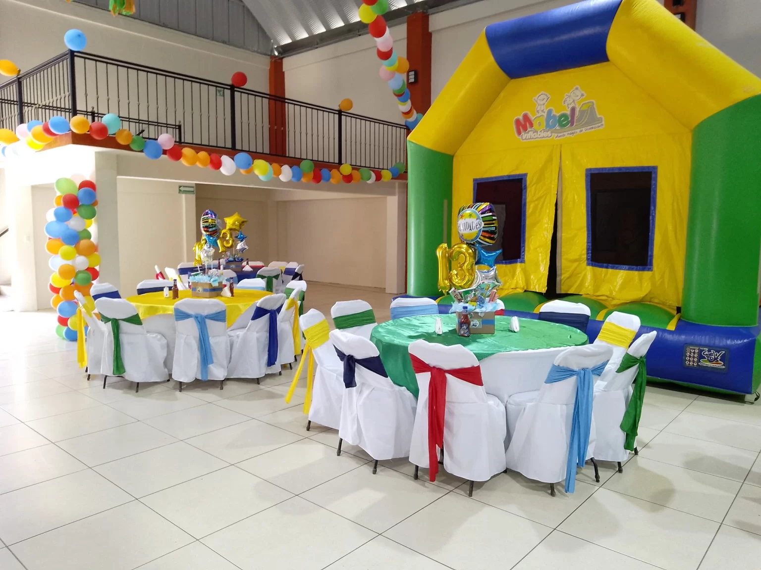 Salón con brincolín inflable, mesas decoradas y globos de colores