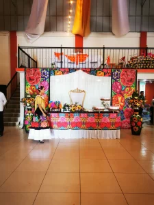 Mujer vestida con traje tradicional del Istmo de Tehuantepec junto a una mesa decorada