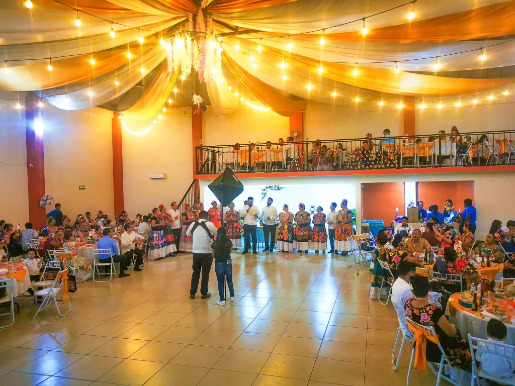 Salón de fiestas con decoración de luces cálidas y temática tradicional, con invitados vestidos en trajes típicos disfrutando del evento