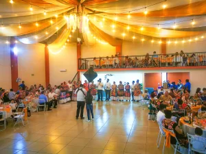 Salón de fiestas con decoración de luces cálidas y temática tradicional, con invitados vestidos en trajes típicos disfrutando del evento