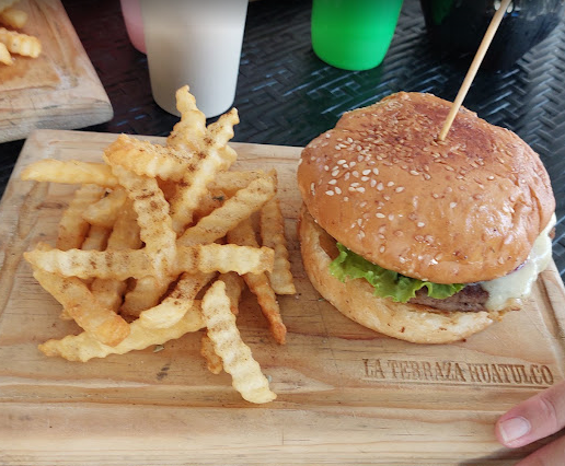 Hamburguesa con papas fritas crujientes servida sobre tabla de madera en Moonlight Café Terraza, Salina Cruz, Oaxaca.