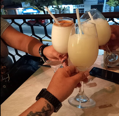 Personas brindando con cocteles en copa en Moonlight Café Terraza, con vista nocturna desde la terraza en Salina Cruz, Oaxaca.