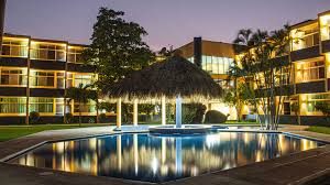 Vista nocturna de la alberca del Hotel Cali con iluminación y palapa central
