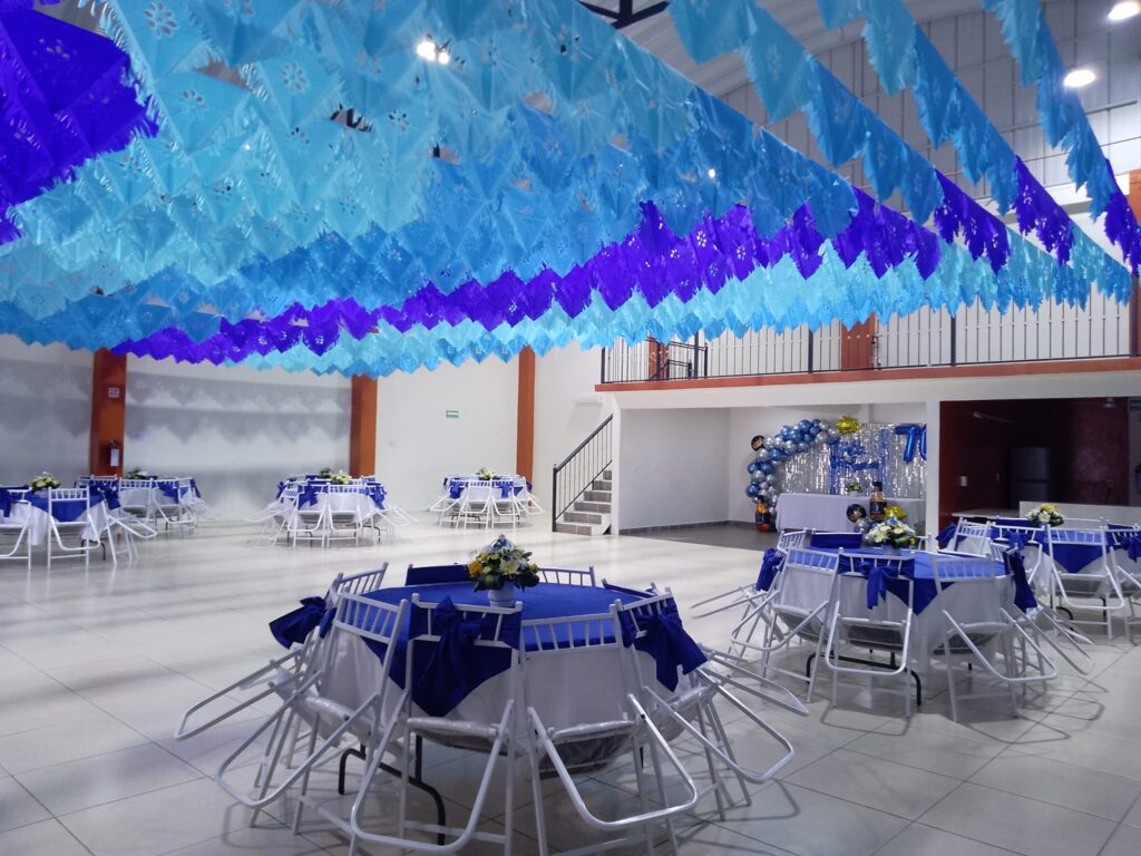 Salón Arboledas Juchitán decorado con papel picado azul y mesas vestidas para una celebración familiar