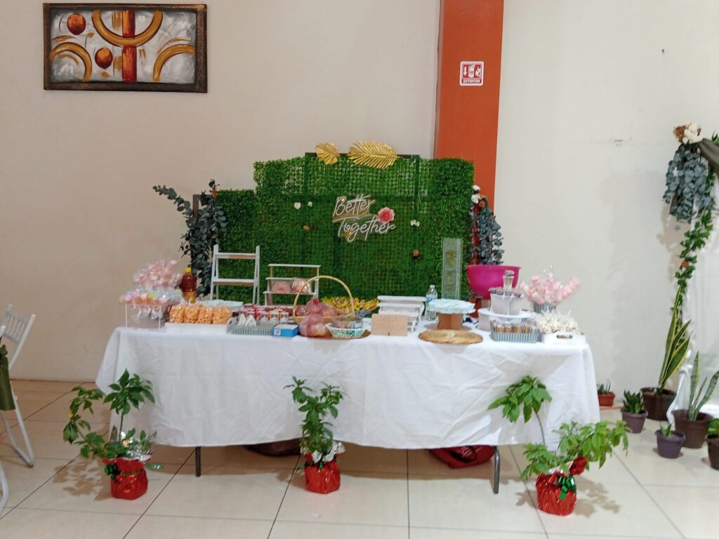 Mesa de postres y golosinas con fondo verde decorativo y plantas en el Salón Arboledas Juchitán