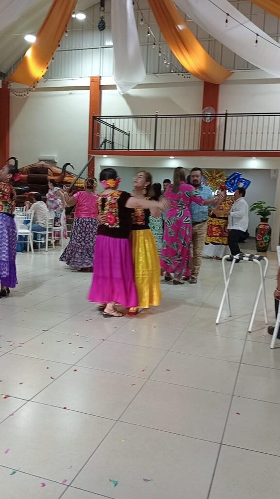 Maestras bailando en salón decorado con telas y luces durante el Día del Maestro. Título: Baile del Día del Maestro en salón de eventos en Juchitán