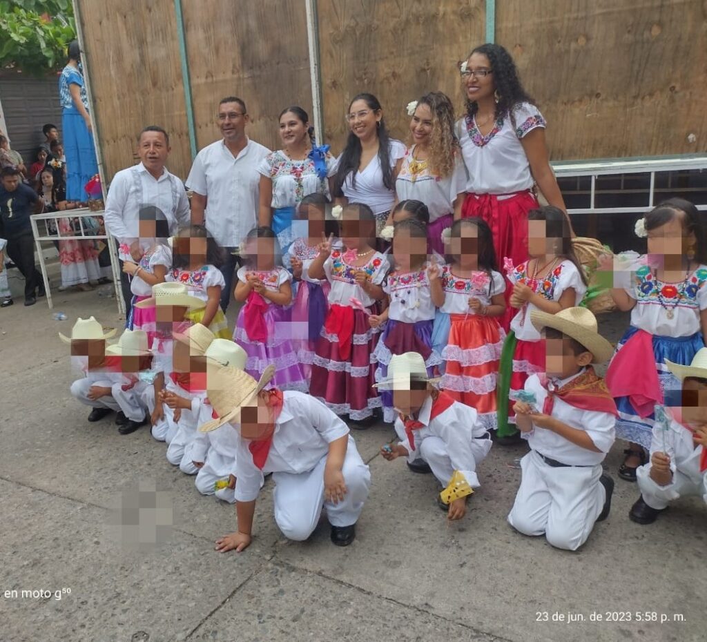 Niños con trajes regionales istmeños posan con docentes en un festival escolar de Juchitán