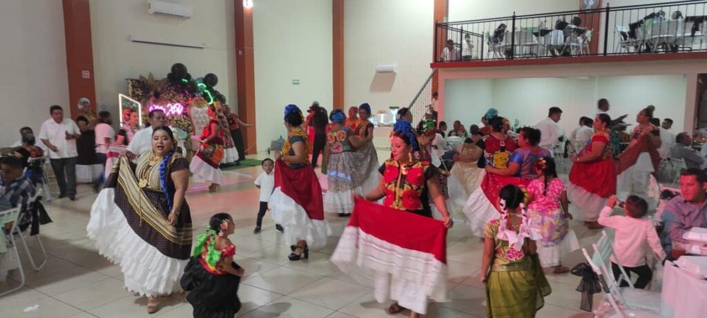 Mujeres con trajes istmeños bailando en salón de eventos, celebración escolar o cultural.